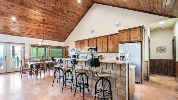 A spacious kitchen with wooden cabinets, a stone island, and bar stools. - Private swimming pool, huge outdoor entertainment area, less than 5-minute drive to THE Frio River (Concan)
