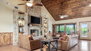 A spacious living room with a stone fireplace, leather sofas, and a television mounted on the wall. - Private swimming pool, huge outdoor entertainment area, less than 5-minute drive to THE Frio River (Concan)