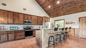 A kitchen with wooden cabinets, a stone island with bar stools, stainless steel appliances, and a rustic ceiling. - Private swimming pool, huge outdoor entertainment area, less than 5-minute drive to THE Frio River (Concan)