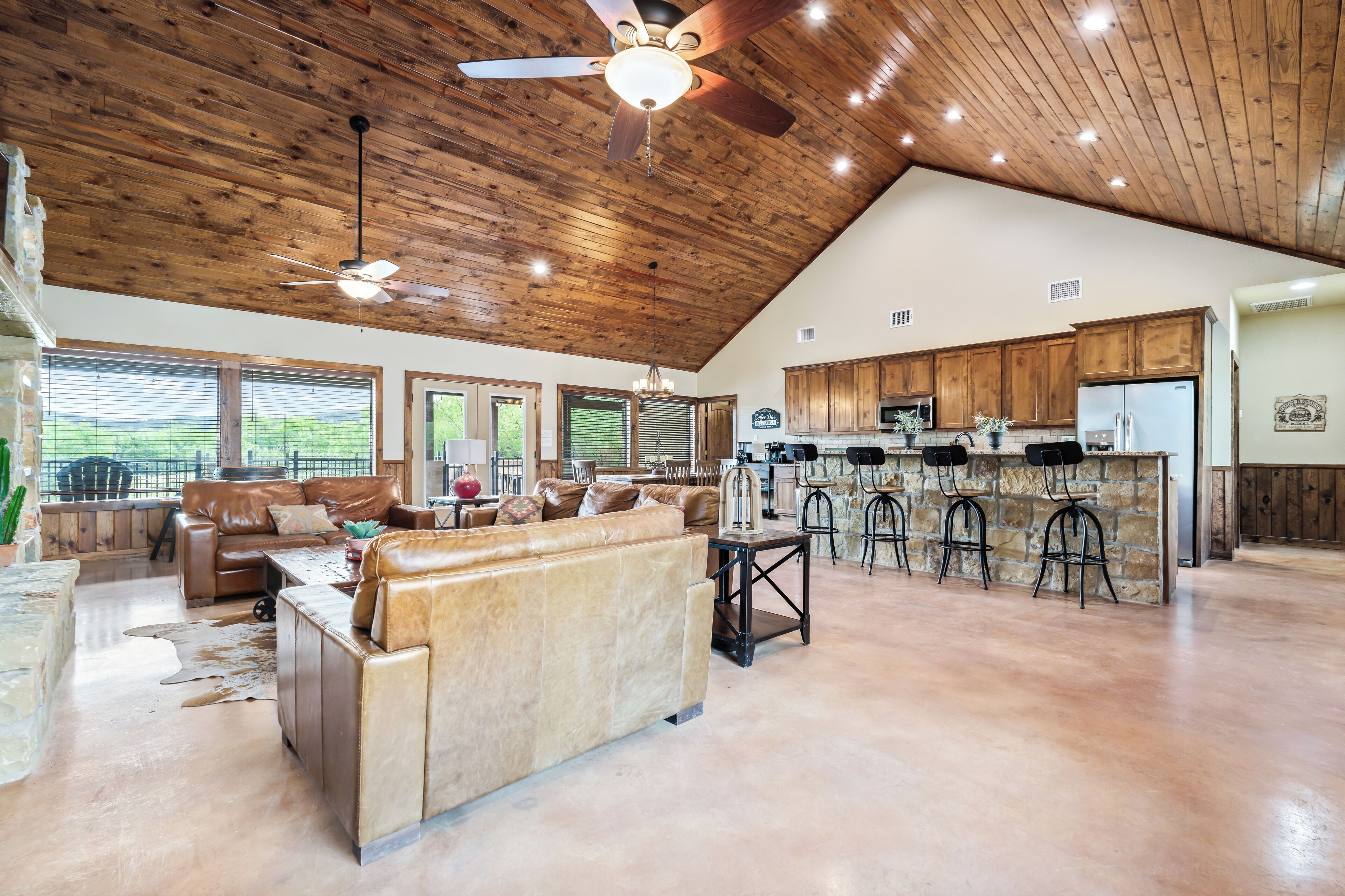 A spacious living area with a high ceiling, wooden beams, a large sofa, and a kitchen with bar stools.
