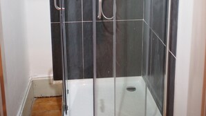 Une cabine de douche fermée par des parois en verre, dotée d’un sol carrelé et d’un receveur blanc.