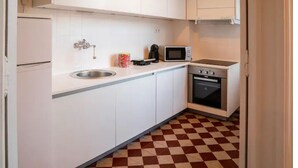 Une cuisine de taille réduite avec des meubles blancs, un évier en acier inoxydable, un four à micro-ondes et un four traditionnel.