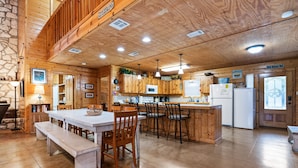 L’intérieur d’un chalet rustique, avec une table à manger en bois, des bancs, un coin cuisine doté de meubles en bois et un mur en pierre.