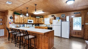 Une cuisine en bois dotée d’un îlot central, de tabourets de bar, d’un four à micro-ondes, d’un réfrigérateur et d’une enseigne indiquant « Old River Rd. »
