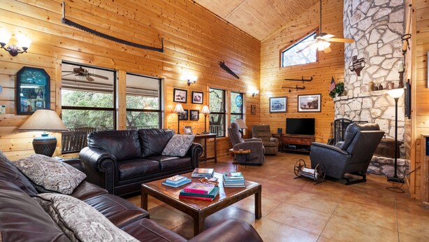 Un intérieur de chalet chaleureux avec des murs en bois, une cheminée en pierre, des meubles en cuir et un grand téléviseur.