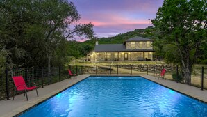 A rectangular swimming pool with a stone house in the background, surrounded by trees and a fence. - Right in the heart of Concan, private swimming pool, epic views & a 2-minute drive to THE Frio River (Concan)