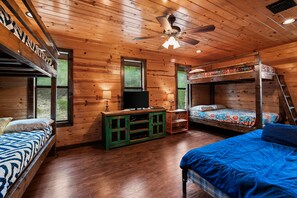 A cabin with wooden walls, a bunk bed, a television, and a ceiling fan.