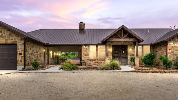 A two-story stone house with a covered front porch, a chimney, and a gravel driveway. - Private pool, volleyball, basketball, outdoor fireplace & less than 5-minute drive to THE Frio River (Concan)