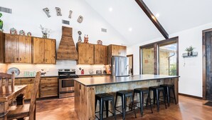 A spacious kitchen with wooden cabinets, a large island with stools, and a stone backsplash. - Private pool, volleyball, basketball, outdoor fireplace & less than 5-minute drive to THE Frio River (Concan)