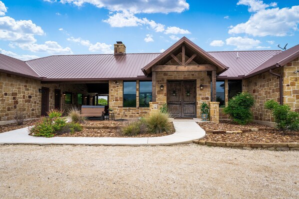 A stone building with a metal roof, a front porch, and a gravel driveway.