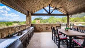 A covered outdoor kitchen area with a stone wall, a sink, and a dining table with benches. - Private pool, volleyball, basketball, outdoor fireplace & less than 5-minute drive to THE Frio River (Concan)