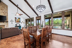 A spacious dining area with a wooden table and chairs, a ceiling fan, and a chandelier.
