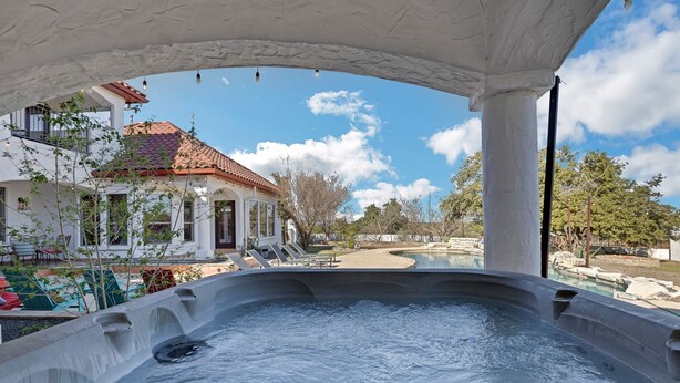 A hot tub area with a view of a house and a pool. - Hill Country Mansion l Pool | Spa (Austin)