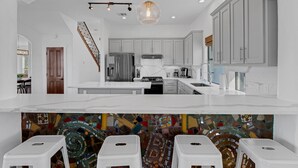 A modern kitchen with white cabinetry, a central island, and a colorful mosaic backsplash. - Hill Country Mansion l Pool | Spa (Austin)