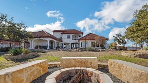 A courtyard with a fire pit, surrounded by stone planters and a large stone bench. - Hill Country Mansion l Pool | Spa (Austin)