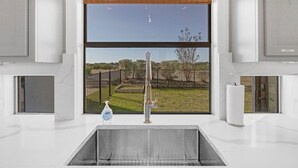 A modern bathroom with a large window, a faucet, and a toilet paper holder. - Hill Country Mansion l Pool | Spa (Austin)