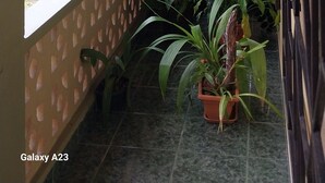 A small, enclosed balcony with a tiled floor, a window with a view of a building, and several potted plants. - Apartamentos Amueblado (Corredores)