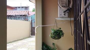 Un balcón pequeño y cerrado con suelo de baldosas, una ventana que ofrece vistas a un edificio y varias plantas en macetas.