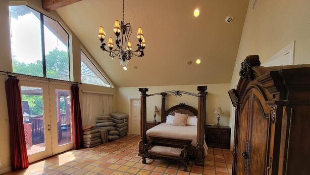 A bedroom with a four-poster bed, a chandelier, and a large window. - Stone House with patio and less than 50 yards to the water. (Clifton)
