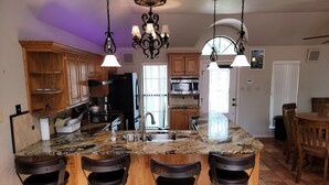 A kitchen with granite countertops, wooden cabinets, a black refrigerator, stainless steel appliances, and a bar area with stools. - Stone House with patio and less than 50 yards to the water. (Clifton)