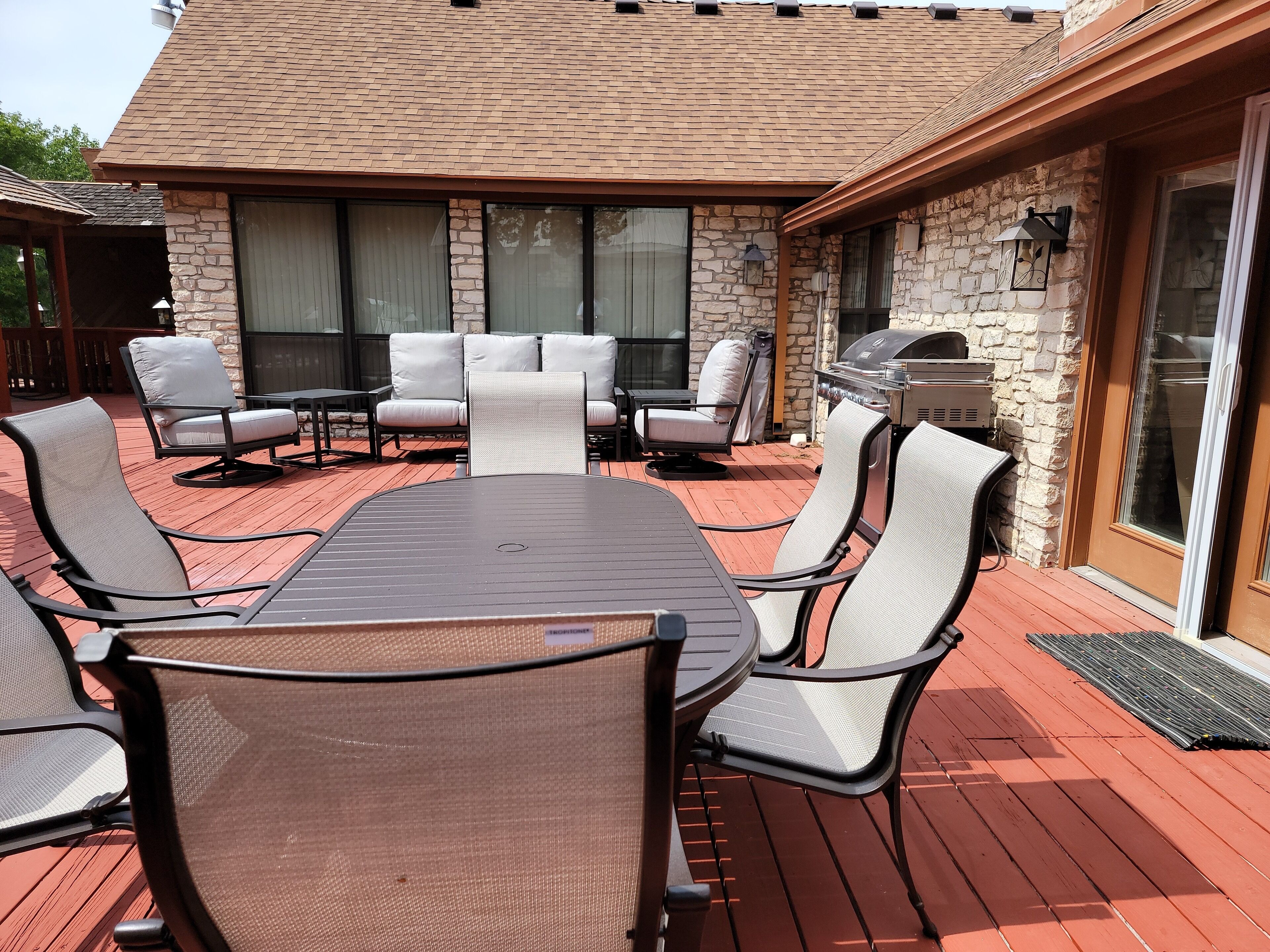 An outdoor patio with a stone wall, a grill, and a seating area with chairs and a table.
