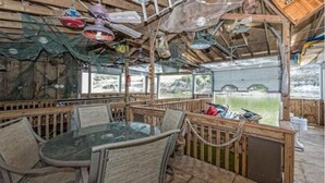 A rustic wooden structure with a glass table and chairs, surrounded by a wooden deck and a view of a natural landscape. - Stone House with patio and less than 50 yards to the water. (Clifton)