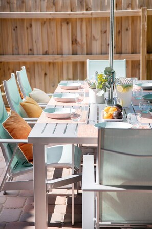 An outdoor dining area with a wooden fence, metal chairs, and a table set with plates, glasses, and a pitcher of lemonade. - Luxury Home - Jacuzzi! Mini-Golf! Ping-Pong! Pets! 2 Desks! Yoga! Beach Gear! (North Palm Beach)