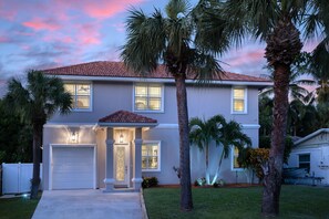 A two-story house with a garage, a well-maintained lawn, and palm trees. - Luxury Home - Jacuzzi! Mini-Golf! Ping-Pong! Pets! 2 Desks! Yoga! Beach Gear! (North Palm Beach)
