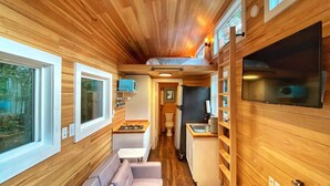 Un intérieur compact aux murs lambrés, comprenant un coin cuisine, un petit espace salon et un téléviseur.