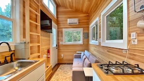 A compact kitchen with wooden walls, a gas stove, a sink, and a built-in bench.