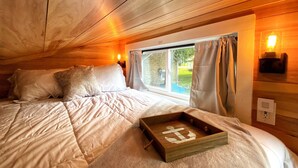 Une chambre confortable avec un plafond en bois, un grand lit recouvert de draps blancs, une fenêtre avec des rideaux et une table de chevet avec une lampe.