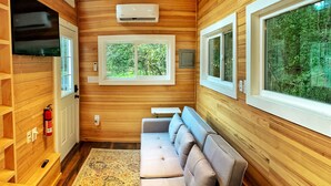 L’intérieur chaleureux d’un chalet avec des murs en bois, un canapé, un téléviseur et de grandes fenêtres donnant sur la forêt.