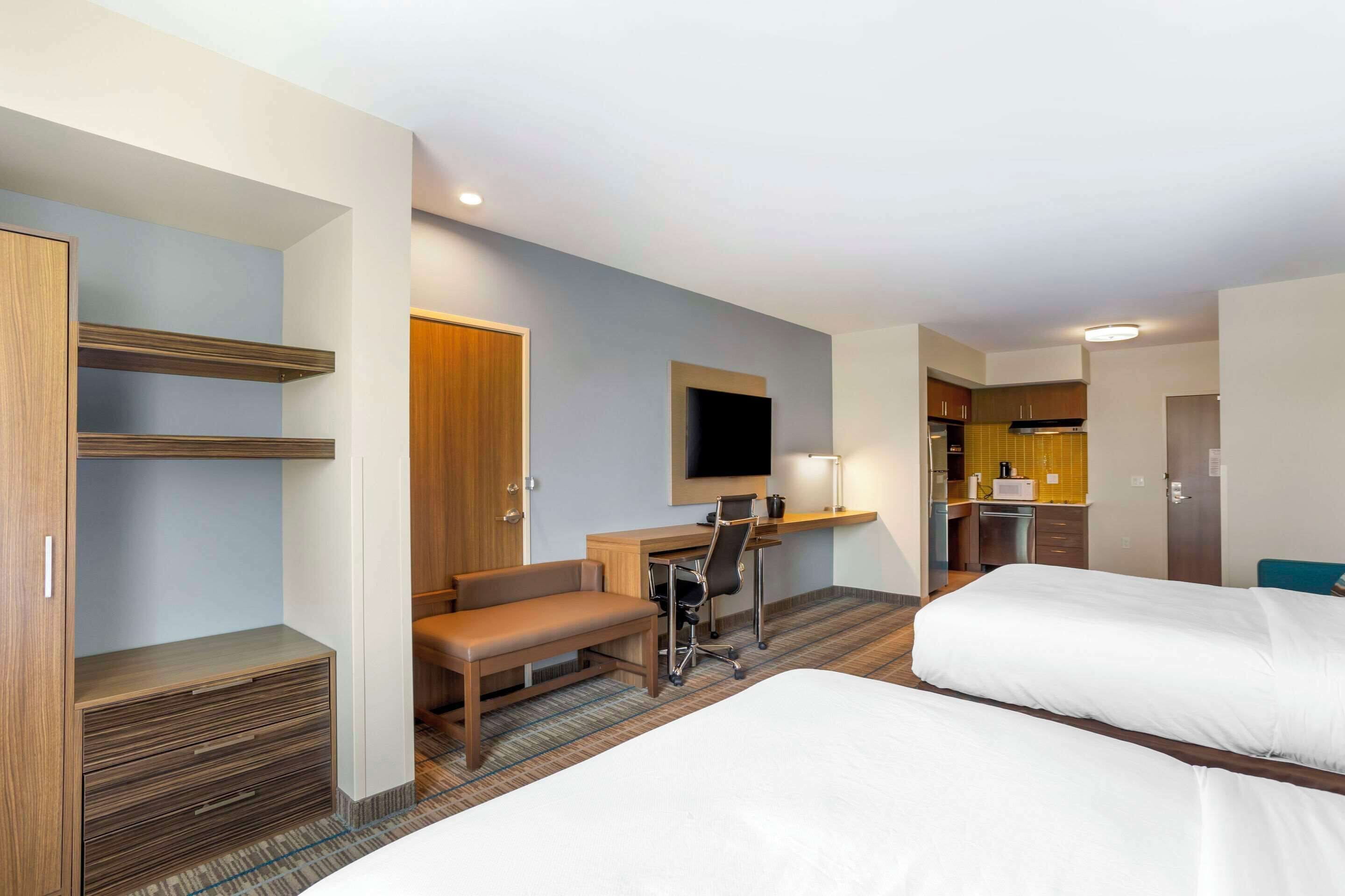 A hotel room with two beds, a desk with a chair, a TV, and a kitchenette.