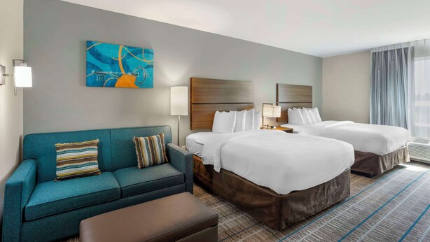 A hotel room with two beds, a sofa, a painting, and a large window with curtains. - MainStay Suites North - Central York (York)