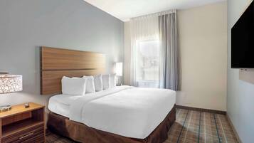 Une chambre d’hôtel avec un grand lit, une tête de lit en bois, une table de chevet avec une lampe et un téléviseur fixé au mur.