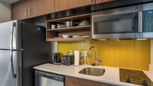 A modern kitchen with stainless steel appliances, wooden cabinets, a yellow-tiled backsplash, and a built-in microwave. - MainStay Suites North - Central York (York)