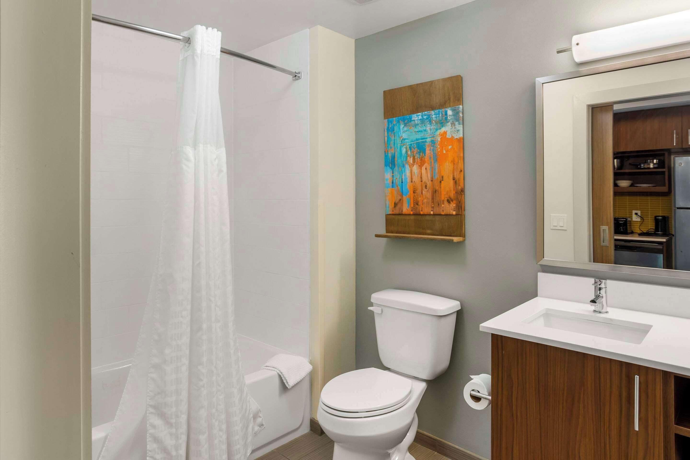 A modern bathroom with a shower, toilet, sink, and a painting on the wall.