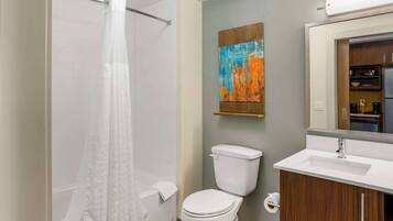 A modern bathroom with a shower, toilet, sink, and a painting on the wall.