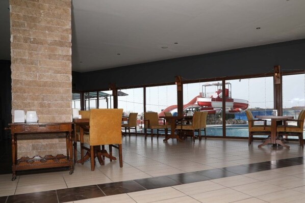 A spacious indoor area with a large window overlooking a pool area, featuring several wooden tables and chairs. - Respiro Park Hotel (Istanbul)