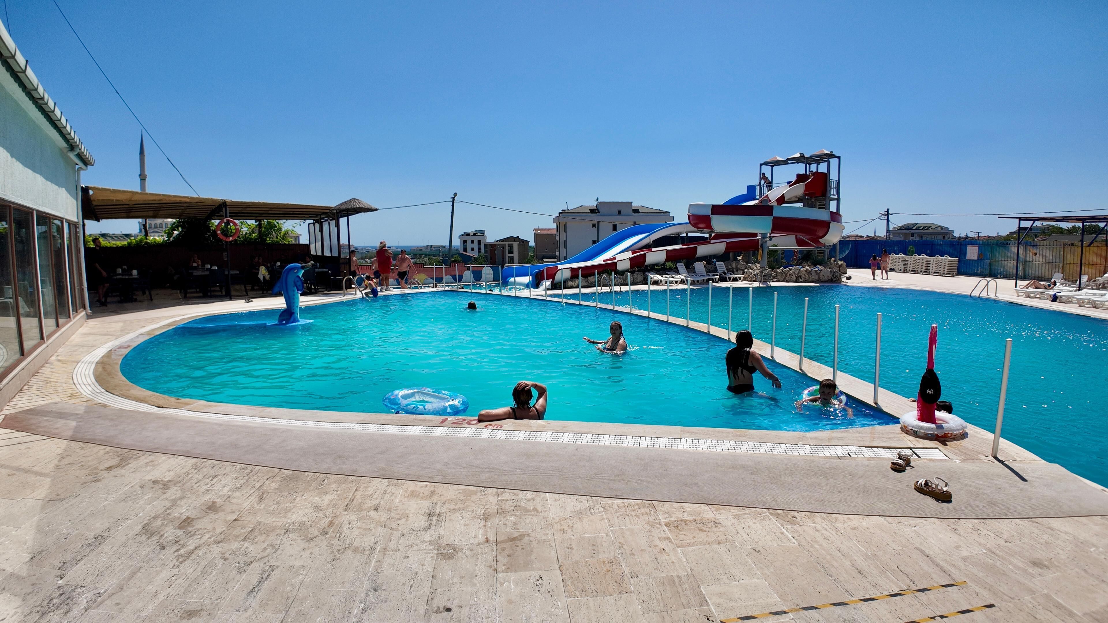 A swimming pool with a water slide, lounge chairs, and a lifeguard stand.