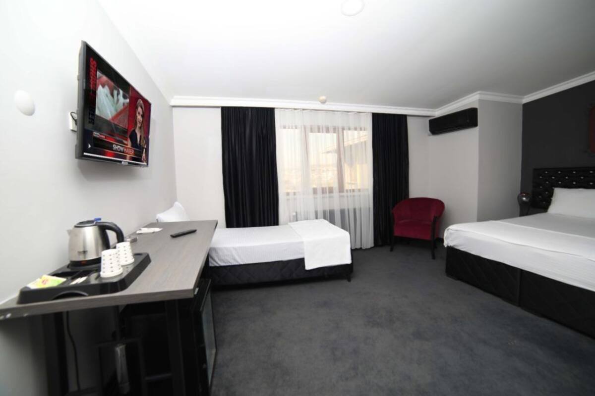 Une chambre d’hôtel avec deux lits, un bureau avec une bouilloire, une télévision et un fauteuil rouge.