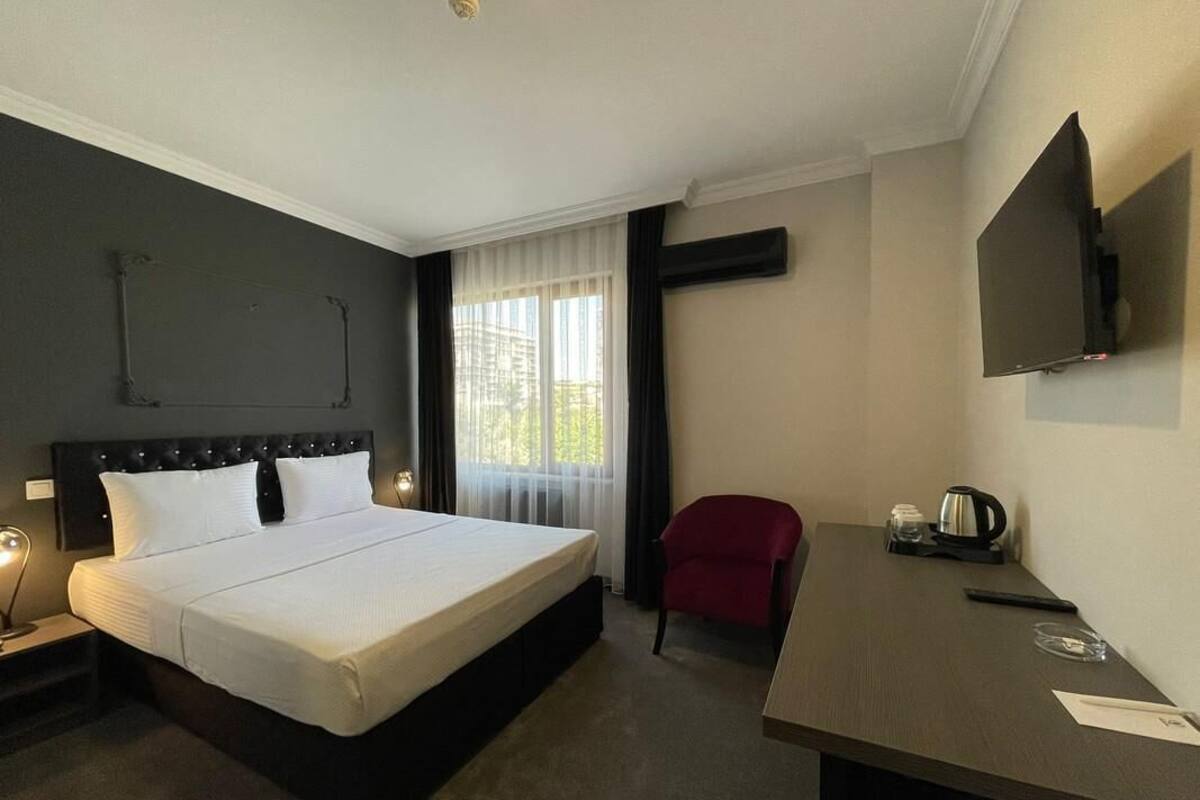 Une chambre d’hôtel avec un grand lit, un bureau avec une chaise, un téléviseur à écran plat et une fenêtre avec des rideaux.