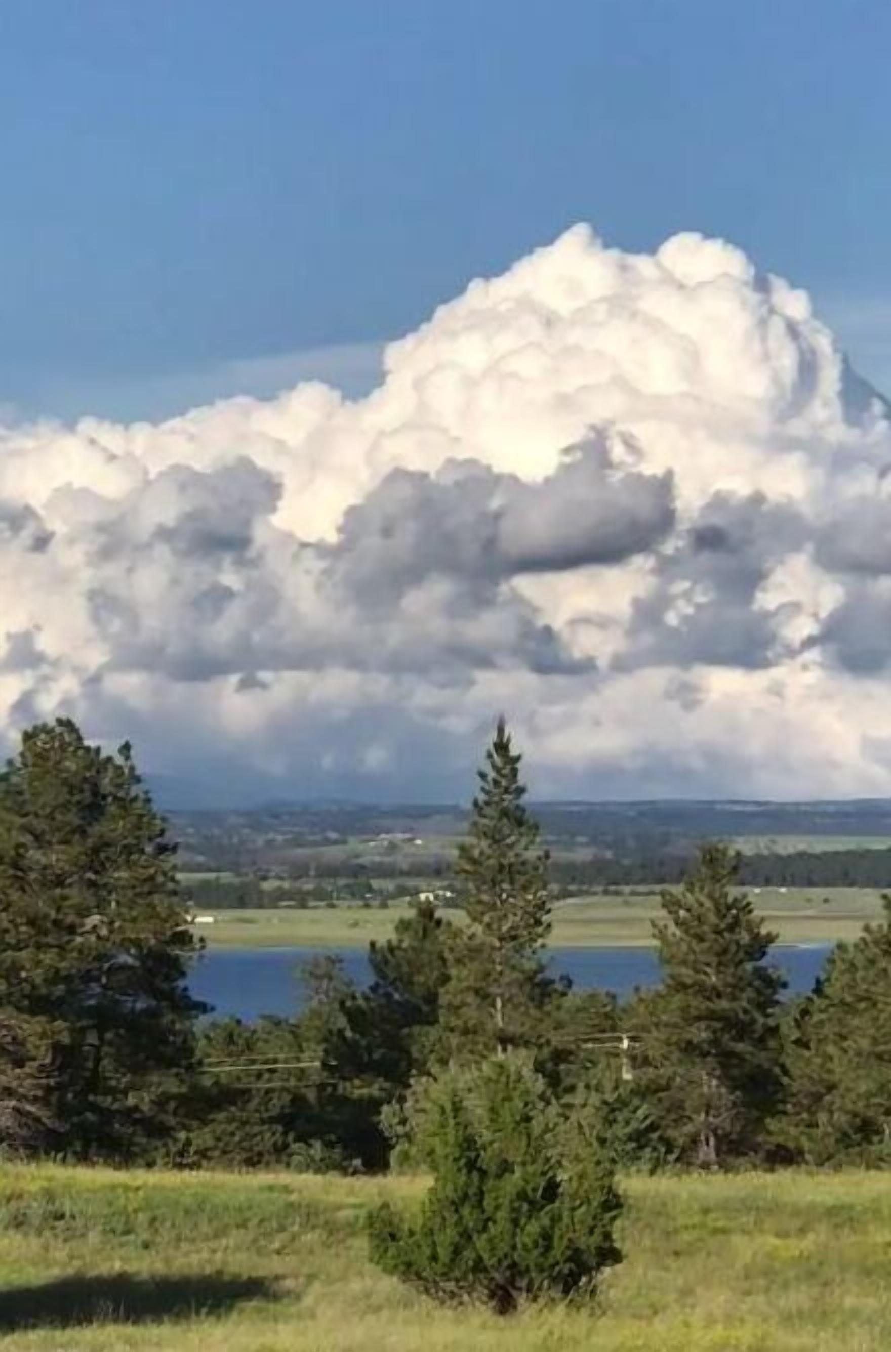 A landscape with a large cloud formation, trees, and a body of water.