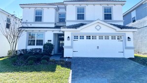A two-story house with a white facade, a garage, and a well-maintained front yard with grass and shrubs.