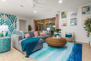 A modern living room with a grey sofa, a round woven ottoman, and a blue abstract rug.