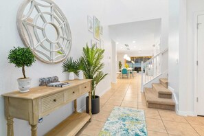 A hallway with a wooden console table, potted plants, a decorative mirror, and a staircase leading to an upper level.
