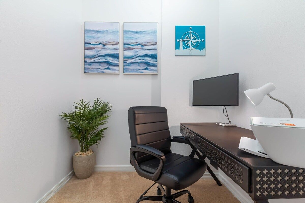 A modern office space with a desk, chair, television, and wall art.