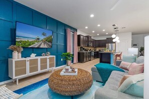 A modern living room with a large TV, a round woven ottoman, and a sofa with cushions.