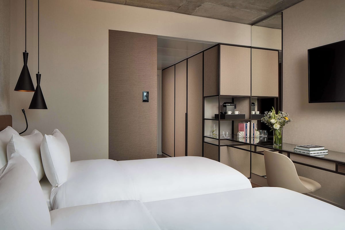 Een moderne hotelkamer met twee bedden, een bureau met stoel, een televisie en een boekenplank.