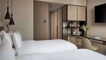Una habitación de hotel moderna con dos camas, un escritorio con silla, televisión y estantería.
